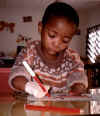 CLICK FOR ENLARGEMENT! Dimpho, a child at the Mogoditshane Rehabilitation Centre, writes with a new pencil holder that CCIer Marjorie Sandercock made for him. Botswana 1993